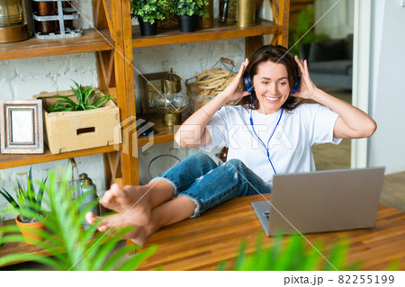 Smiling woman in headset in front of a laptop monitor at home. She puts her feet on the table and vividly discusses the latest gossip with her friend. Smiling woman in headset in front of a laptop monitor at home. She puts her feet on the table and vividly discusses the latest gossip with her friend. 82255199