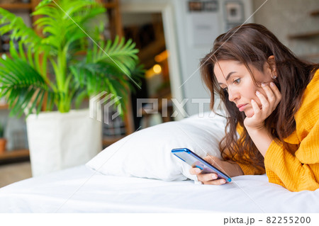 Sad woman lies in bed with cell phone. She woke up and was checking social media posts. Sad woman lies in bed with cell phone. She woke up and was checking social media posts. 82255200