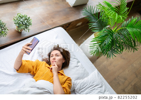 Virtual love - woman lies in bed with cell phone. Online call to virtual boyfriend. View from the top. 82255202