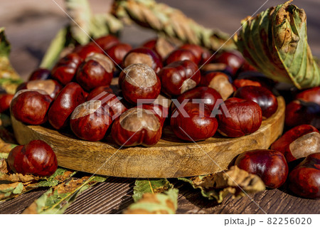 Chestnuts in a plate with dry leaves on a brown wooden table. Autumn still life with bright horse chestnuts on wooden background 82256020