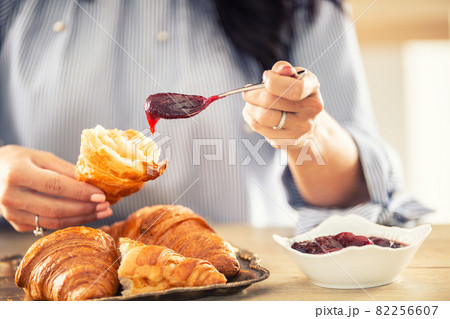 Female hands put jam onto a halved croissant in the morning 82256607