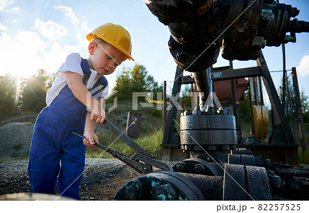 Caucasian blonde boy with instrument fixing drilling rig during time for learning at petroleum station in nature environment, young man in professional uniform studying engineering at oil platform 82257525