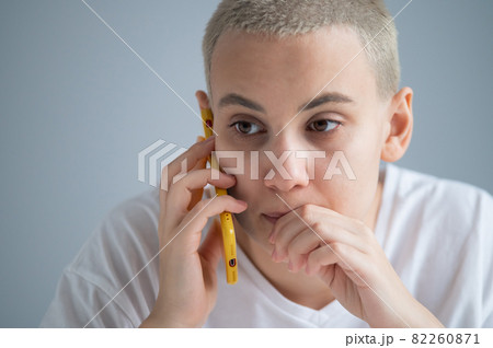 A pensive young woman with a short haircut talks thoughtfully on a mobile phone on a white background 82260871