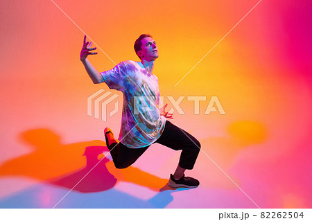 Top view image of young artistic man dancing hip-hop isolated over gradient yellow pink studio background in neon light Top view image of young artistic man dancing hip-hop isolated over gradient yellow pink studio background in neon light 82262504