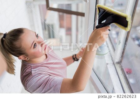 Beautiful young housewife in working clothes washing windows by professional tools at home. Beautiful young housewife in working clothes washing windows by professional tools at home. 82262623