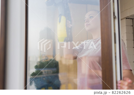 Beautiful young housewife in working clothes washing windows by professional tools at home. Beautiful young housewife in working clothes washing windows by professional tools at home. 82262626