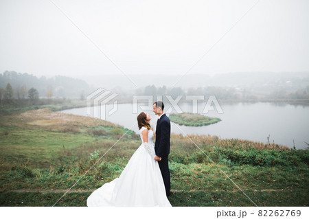 Romantic, fairytale, happy newlywed couple hugging and kissing in a park, trees in background Romantic, fairytale, happy newlywed couple hugging and kissing in a park, trees in background 82262769