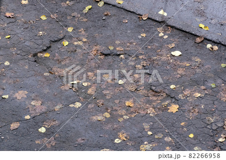 Pits in the asphalt and yellow autumn leaves. The old road. Poor road surface. Top view. 82266958