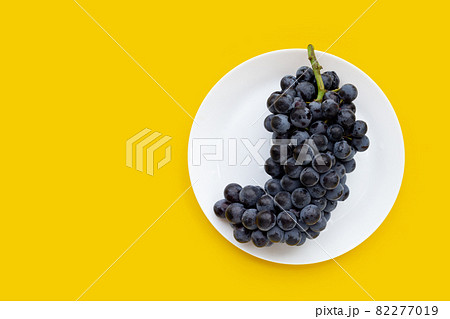 Fresh black grapes in white plate on yellow background. 82277019
