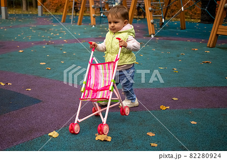 cute toddler kid carries a baby stroller for a walk in the autumn park 82280924
