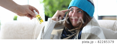 Marijuana oil in hand closeup with sick woman in hat and scarf under blanket on background Marijuana oil in hand closeup with sick woman in hat and scarf under blanket on background 82285379