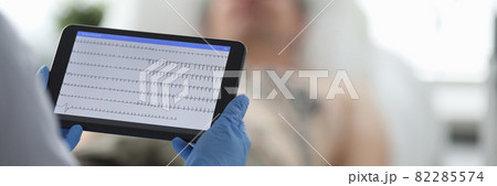 Doctor with ecg monitor stands in front of patient in background Doctor with ecg monitor stands in front of patient in background 82285574