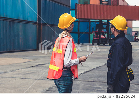 Industrial worker works with co-worker at overseas shipping container yard Industrial worker works with co-worker at overseas shipping container yard 82285624