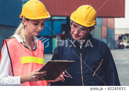 Industrial worker works with co-worker at overseas shipping container yard Industrial worker works with co-worker at overseas shipping container yard 82285652