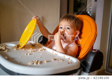 adorable baby plays with a plastic plate at the table. little child indulges in a baby chair after eating adorable baby plays with a plastic plate at the table. little child indulges in a baby chair after eating 82286100