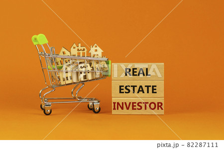 Real estate investor symbol. Wooden blocks, words 'Real estate investor' on beautiful orange background. Shopping cart with miniature wooden houses. Business, Real estate investor concept. Copy space. Real estate investor symbol. Wooden blocks, words 'Real estate investor' on beautiful orange background. Shopping cart with miniature wooden houses. Business, Real estate investor concept. Copy space. 82287111