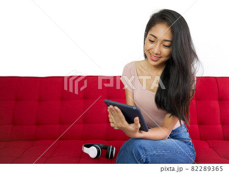 Asian teenager use the application to connect headphones to tablet computer on the red sofa to relax in the living room. Enjoy leisure weekend at home. Stress free concept Asian teenager use the application to connect headphones to tablet computer on the red sofa to relax in the living room. Enjoy leisure weekend at home. Stress free concept 82289365