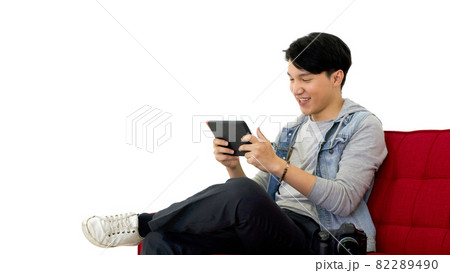 Young asian photographer with a smile view pictures taken on the tablet computer screen while sitting on a red sofa. Working atmosphere in the photo studio 82289490