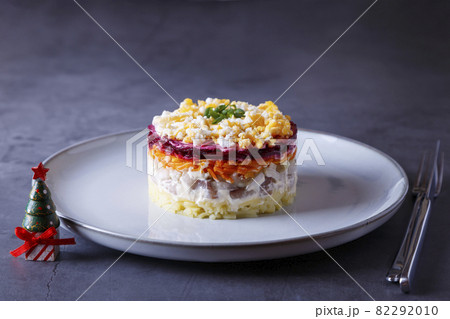 Herring salad under a fur coat. Traditional Russian multilayered salad from herring, beets, potatoes, carrots and eggs. Close-up, grey background, miniature Christmas tree. Herring salad under a fur coat. Traditional Russian multilayered salad from herring, beets, potatoes, carrots and eggs. Close-up, grey background, miniature Christmas tree. 82292010