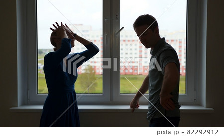 Quarantine concept. Silhouette of young spouses swearing on the background of the window of their apartment. 82292912