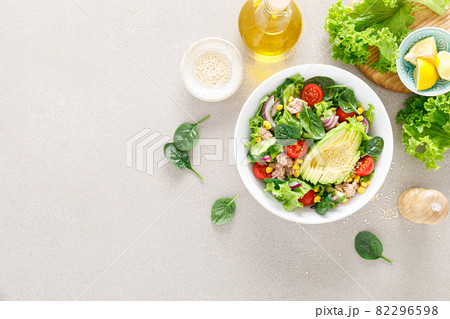 Avocado and tuna fresh vegetable salad with tomato, cucumber corn, onion, lettuce and spinach. Healthy and detox food concept. Ketogenic diet. Buddha bowl dish on light background, top view 82296598