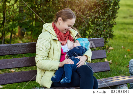 Smiling woman is breastfeeding baby in park. Smiling woman is breastfeeding baby in park. 82298845