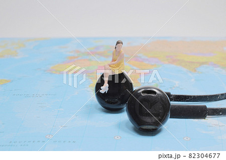 a figure sitting on white earphone on world map. a figure sitting on white earphone on world map. 82304677