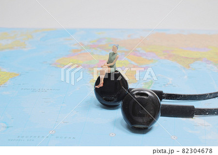a figure sitting on white earphone on world map. 82304678