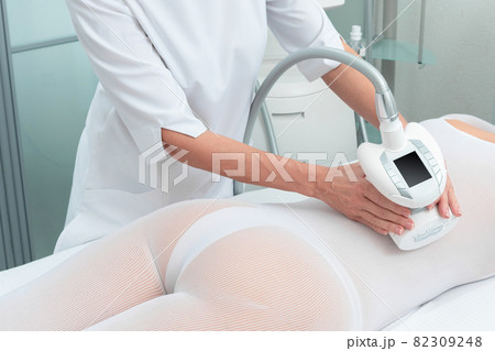 Woman in special white suit getting anti cellulite massage in a spa salon. LPG, and body contouring treatment in clinic. 82309248