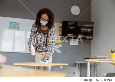 Teacher holding disinfectant and standing in classroom 82310498