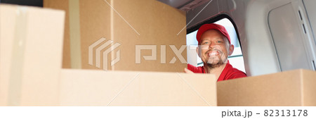 Smiling male courier pulls out cardboard box from car Smiling male courier pulls out cardboard box from car 82313178