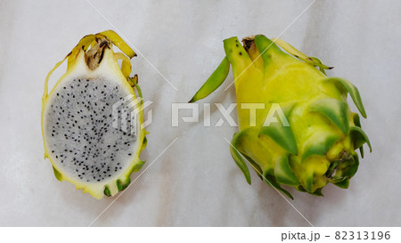 Top view of two yellow dragon fruit. One with skin, another one cut into half with the flesh inside exposed. Top view of two yellow dragon fruit. One with skin, another one cut into half with the flesh inside exposed. 82313196