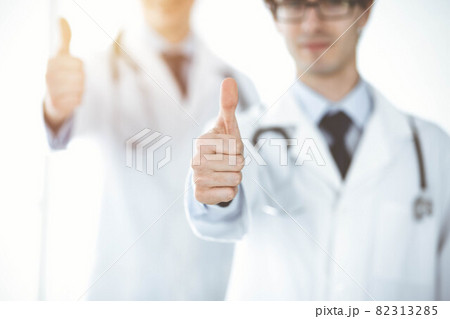 Two male doctors standing as a team and showing thumbs up as a symbol of the best service for patients in sunny clinic. Medicine concept 82313285