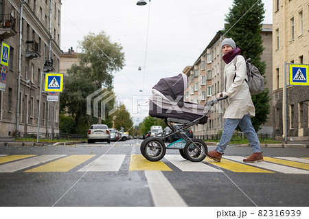 Woman with stroller on crosswalk crossing the road looking aside checking cars. 82316939