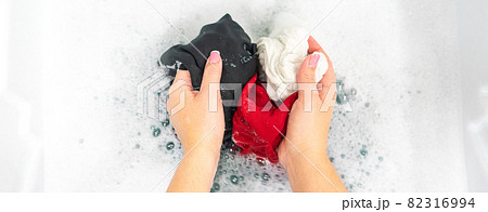 Panorama of female hands washing black, red and white clothes in white foam Panorama of female hands washing black, red and white clothes in white foam 82316994