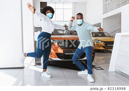 Young Afro couple in face masks dancing, celebrating purchase of new car at auto dealership during covid lockdown 82318998