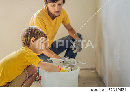 Man with his son makes repairs at home, he teaches children to plaster the walls with a spatula in his hands Man with his son makes repairs at home, he teaches children to plaster the walls with a spatula in his hands 82319621