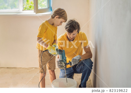 Man with his son makes repairs at home, he teaches children to plaster the walls with a spatula in his hands Man with his son makes repairs at home, he teaches children to plaster the walls with a spatula in his hands 82319622