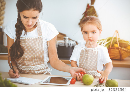Happy woman and her daughter are searching for new recipes for a family feasting, sunny kitchen. Christmas, New year, Thanksgiving, Anniversary, Mothers Day. Healthy meal cooking concept 82321564