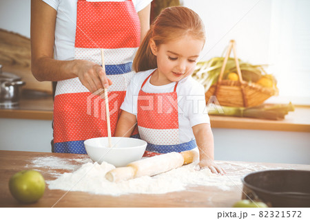 Happy woman and her daughter are kneading the dough and baking cookies for a delicious family feasting in sunny kitchen. Christmas, New year, Thanksgiving, Anniversary, Mothers Day. Healthy meal Happy woman and her daughter are kneading the dough and baking cookies for a delicious family feasting in sunny kitchen. Christmas, New year, Thanksgiving, Anniversary, Mothers Day. Healthy meal 82321572