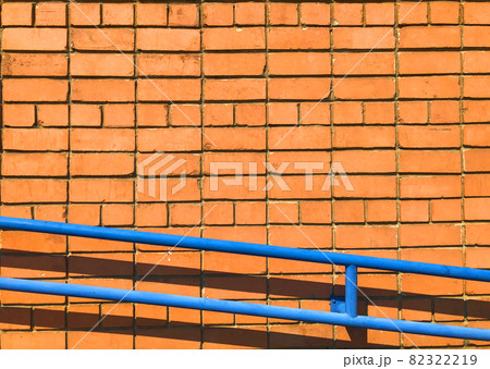 Orange brick wall. Textured background with copy space for design work. Material pattern. Reddish-brown brick blocks facade with blue handrail. Industrial wallpaper with brickwork. No people Orange brick wall. Textured background with copy space for design work. Material pattern. Reddish-brown brick blocks facade with blue handrail. Industrial wallpaper with brickwork. No people 82322219
