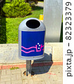 Blue metal trash can with ashtray near the lawn. Urban environmental care concept. Modern stylish waste bin on tiled brick sidewalk as an element of city infrastructure. Dnipro, Ukraine, 2021 82323379