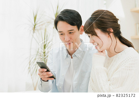 ソファーに座ってスマホを見る若い夫婦 ソファーに座ってスマホを見る若い夫婦 82325172