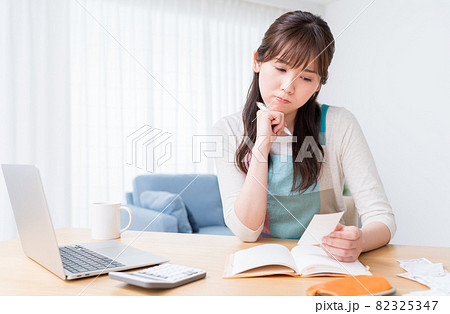 レシートを確認しながら家計簿をつけ家計のやりくりに悩む女性 レシートを確認しながら家計簿をつけ家計のやりくりに悩む女性 82325347