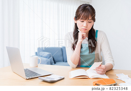 レシートを確認しながら家計簿をつけ家計のやりくりに悩む女性 レシートを確認しながら家計簿をつけ家計のやりくりに悩む女性 82325348