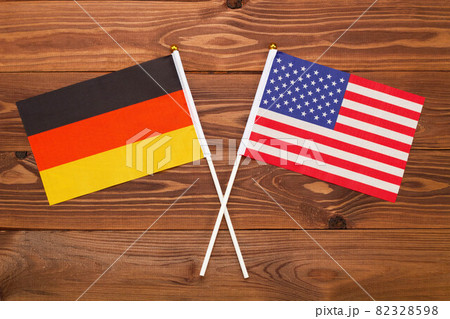 The flag of Germany and the flag of USA are crossed with each other on a brown background with a wood texture. Top view. Close Up The flag of Germany and the flag of USA are crossed with each other on a brown background with a wood texture. Top view. Close Up 82328598