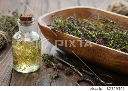Bottle of thyme essential oil or infusion, wooden bowl filled with dried thymus serpyllum plants,  healthy thyme flowers on wooden table. Alternative medicine. 82329501