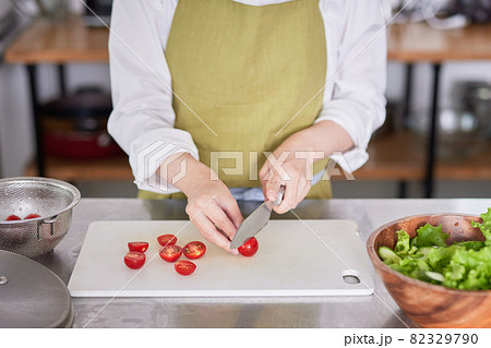 ミニトマトを包丁で切るエプロン姿の若い女性 ミニトマトを包丁で切るエプロン姿の若い女性 82329790