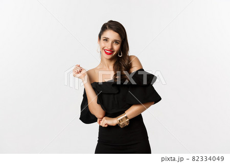 Fashion and beauty. Woman celebrating and dancing in black dress, having fun and smiling, standing over white background 82334049