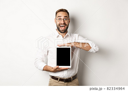 Excited man showing digital tablet screen, smiling amazed, standing over white background Excited man showing digital tablet screen, smiling amazed, standing over white background 82334964
